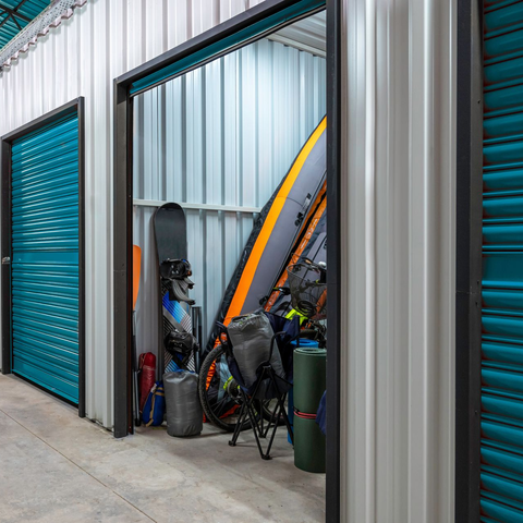 Porte d'un box de stockage rempli de vélos, de planches et d'équipements à côté de portes sectionnelles bleues
