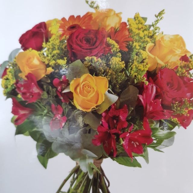 Un ramo de flores rojas, amarillas y naranjas con hojas verdes.