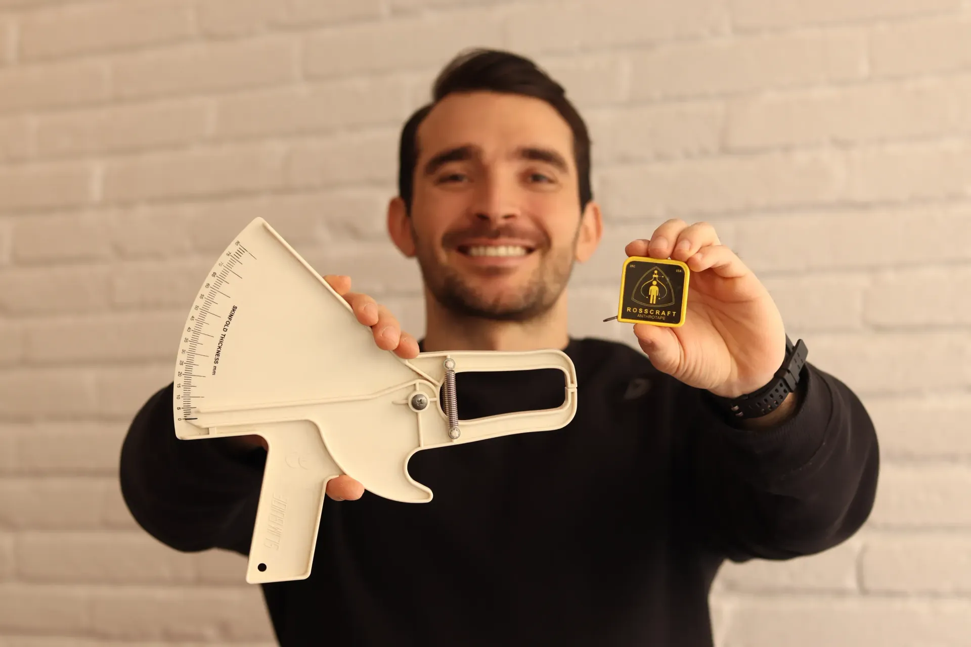 Hombre sonriendo, sosteniendo un megáfono blanco y un pequeño objeto cuadrado amarillo.