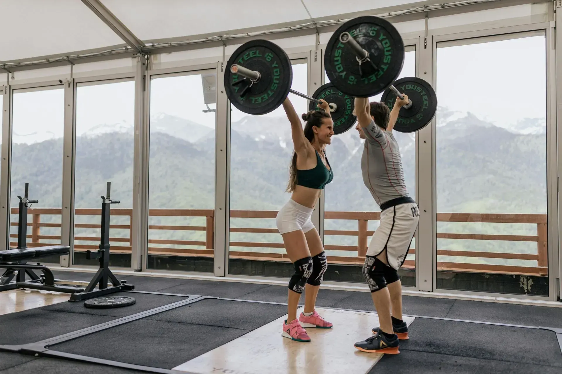 Dos personas levantando pesas en un gimnasio con vistas a la montaña.