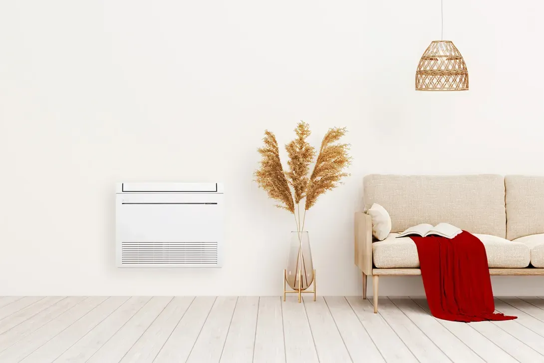 Climatiseur mural blanc dans un salon avec un canapé beige, une couverture rouge et un vase décoratif.