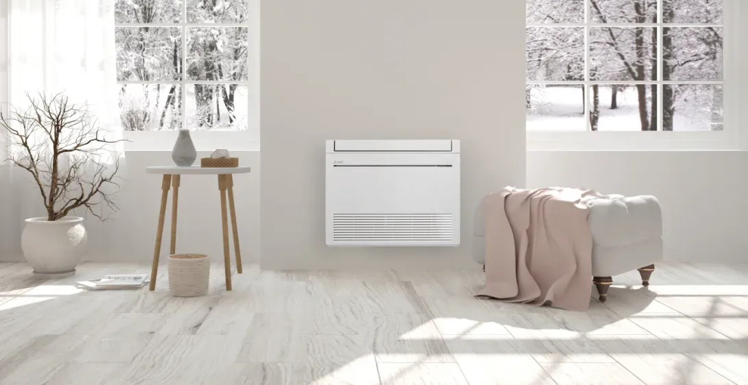 Un radiateur mural blanc dans une pièce avec des fenêtres donnant sur l'hiver, une petite table et une couverture sur une banquette rembourrée.