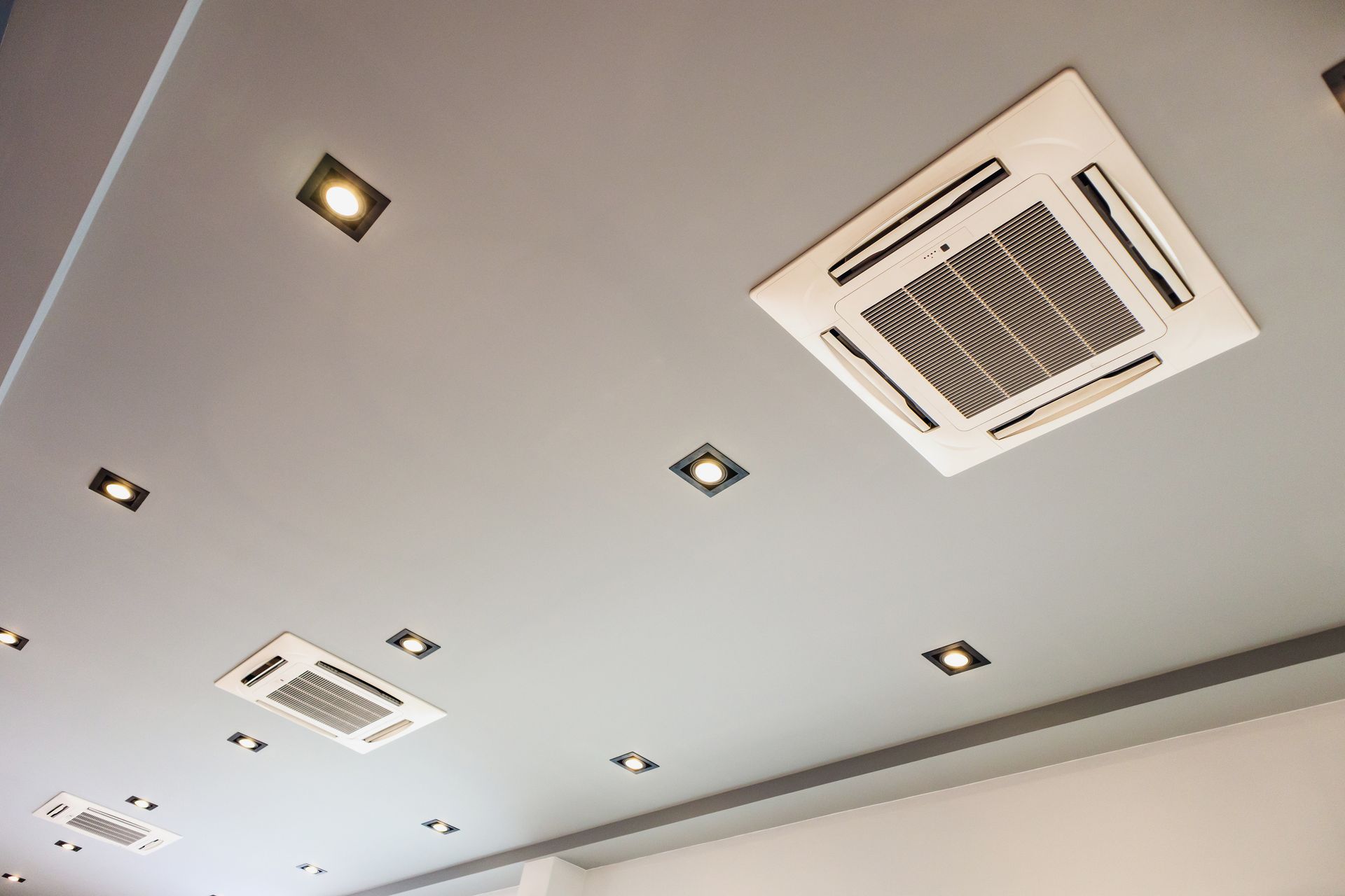 Plafond blanc avec éclairage encastré et deux unités de climatisation fixées au plafond.