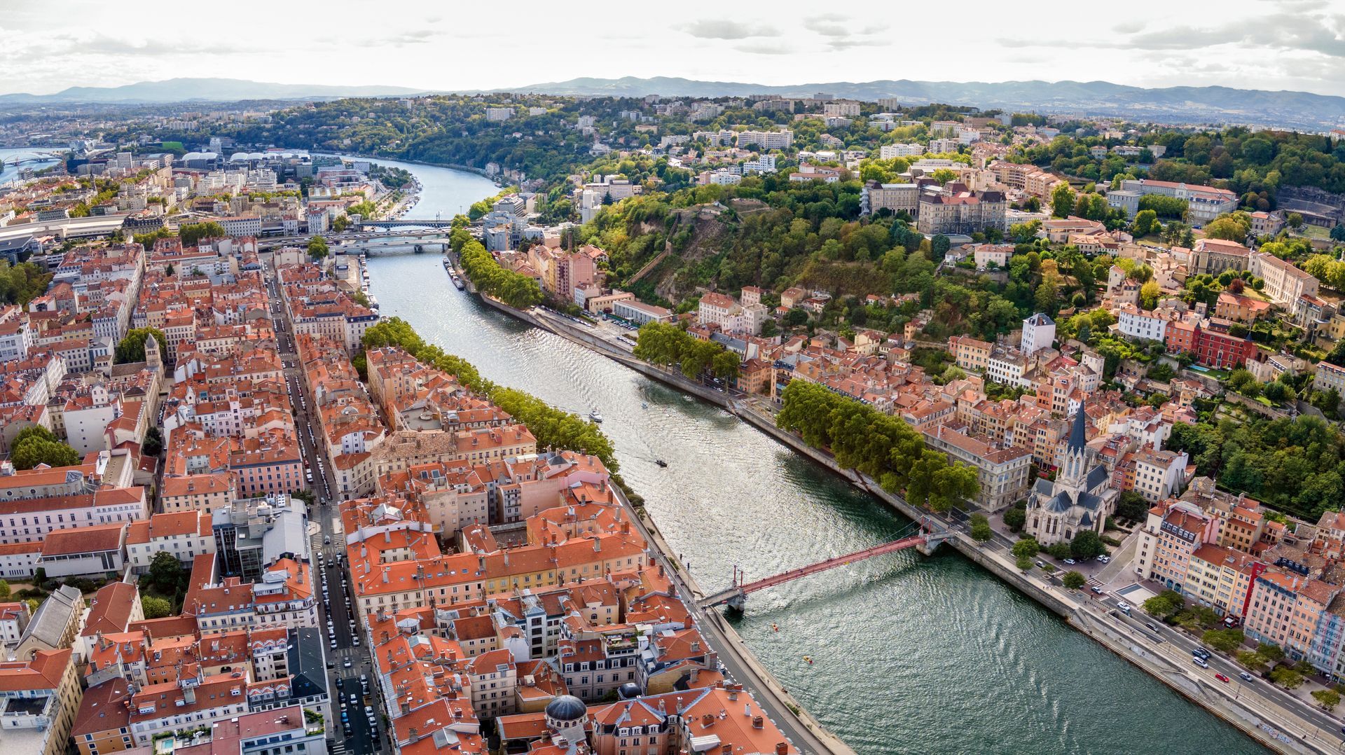 Vue aérienne de Lyon, en France, avec ses bâtiments, ses rivières, ses ponts et sa végétation luxuriante sous un ciel dégagé.