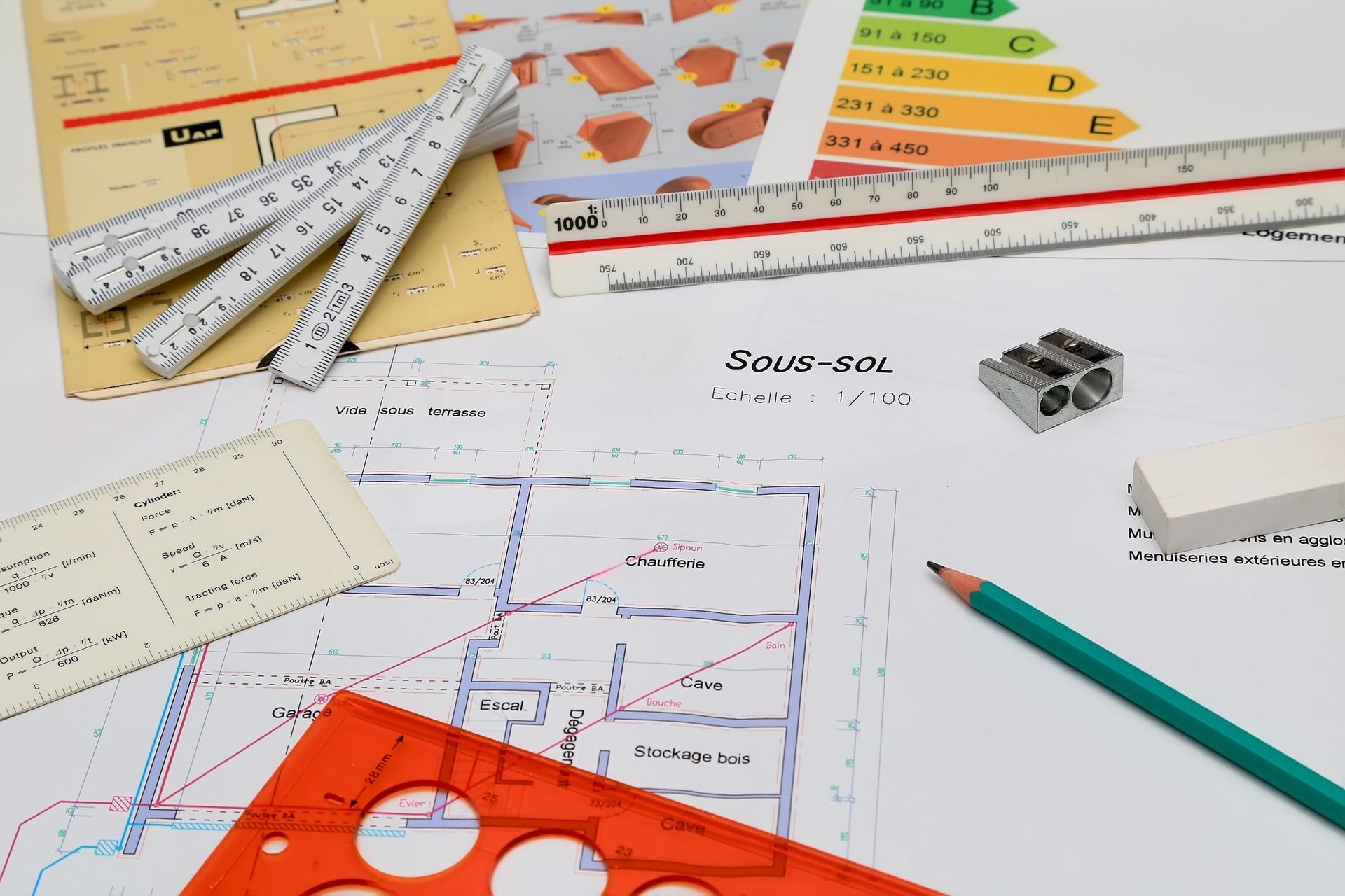 Bureau d'architecte avec plans, règles, crayon, gomme et étiquette d'efficacité énergétique, suggérant un processus de planification ou de conception.