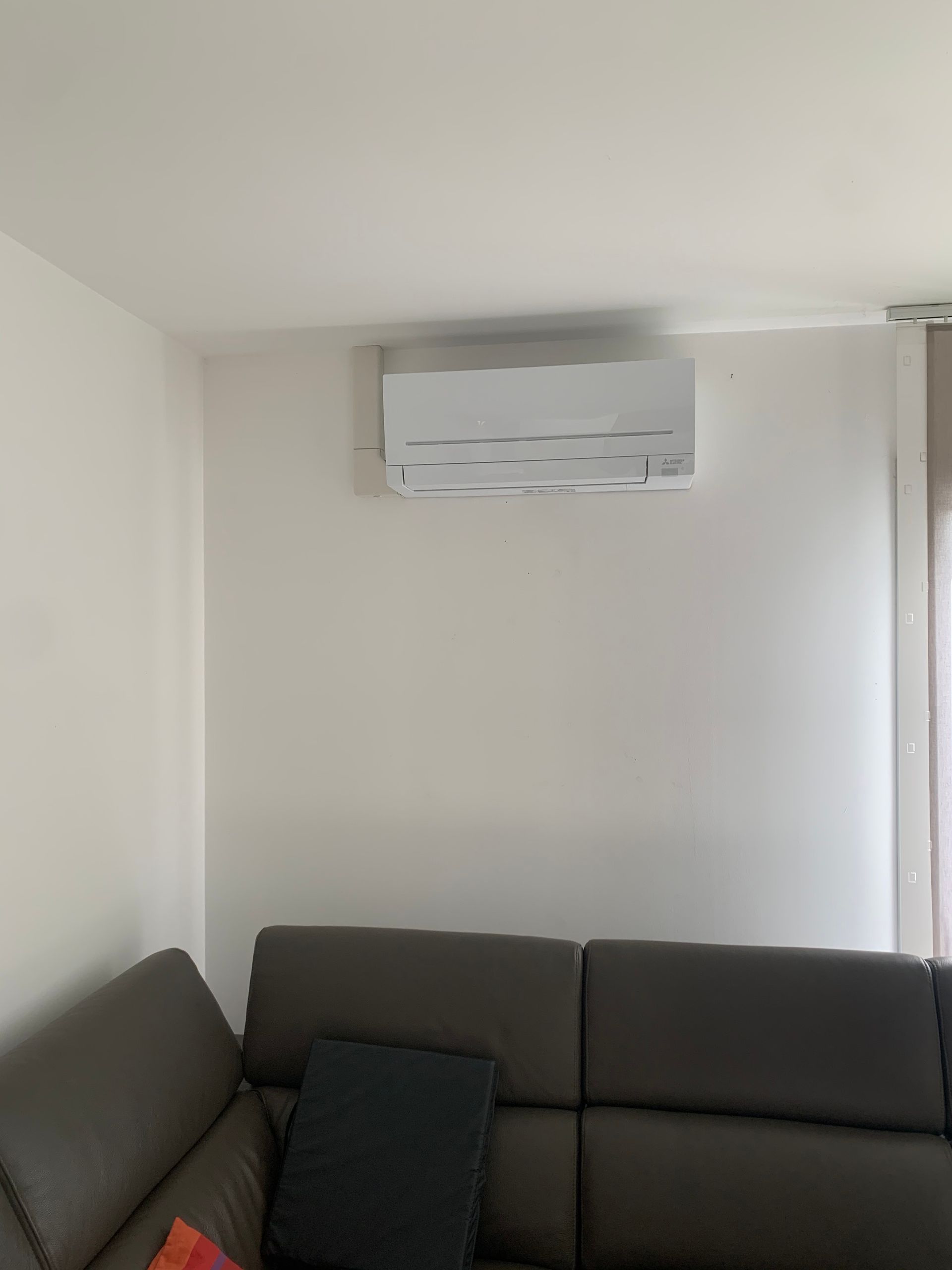 Mur blanc avec un climatiseur au-dessus d'un canapé gris foncé.