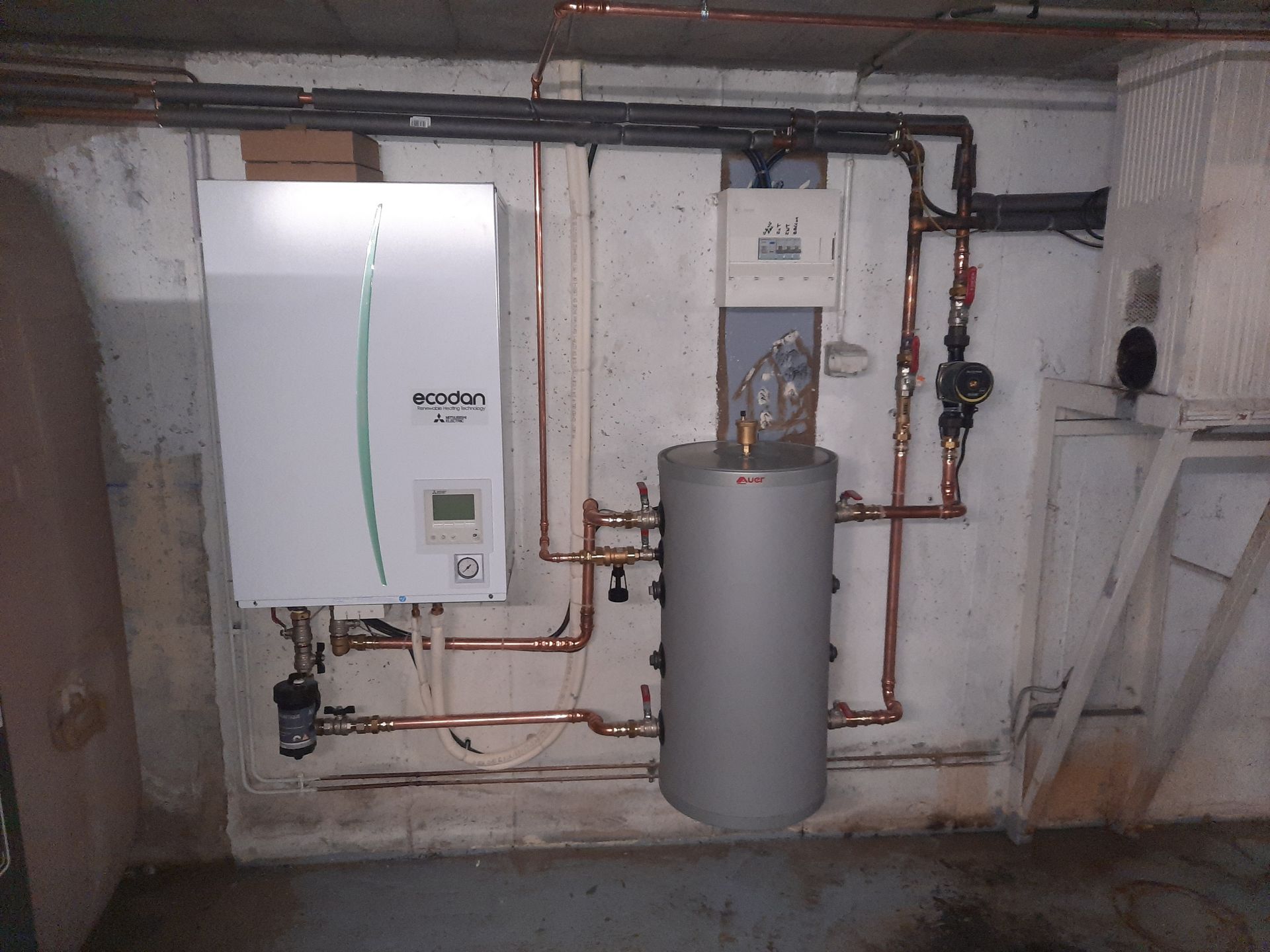 Chauffe-eau blanc et réservoir attenant avec tuyauterie en cuivre, installés dans un sous-sol.