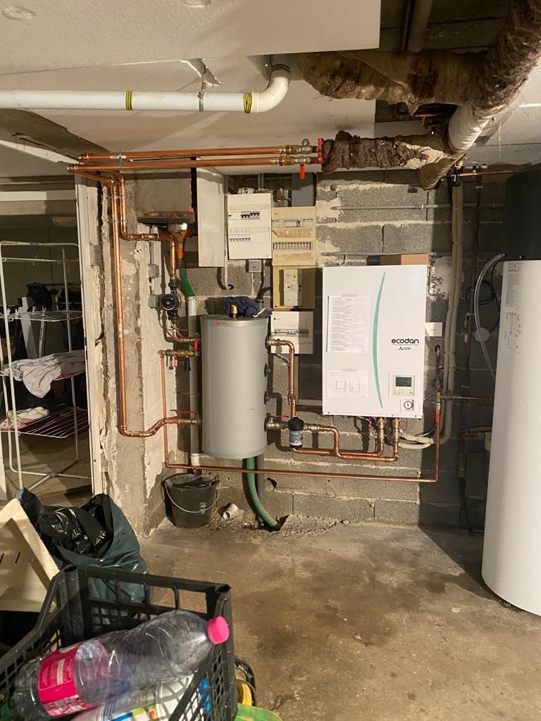 Sous-sol avec les composants du système de chauffage, comprenant un chauffe-eau, une chaudière et des tuyaux en cuivre.