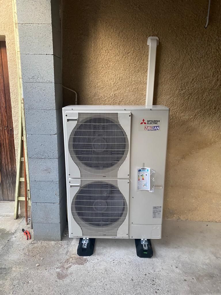 Unité de pompe à chaleur extérieure contre un mur. Blanche et noire, avec une grille d'aération.