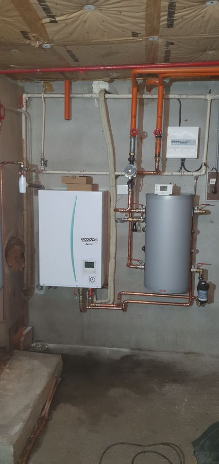 Une chaudière, un chauffe-eau et des tuyaux en cuivre sur un mur en béton.