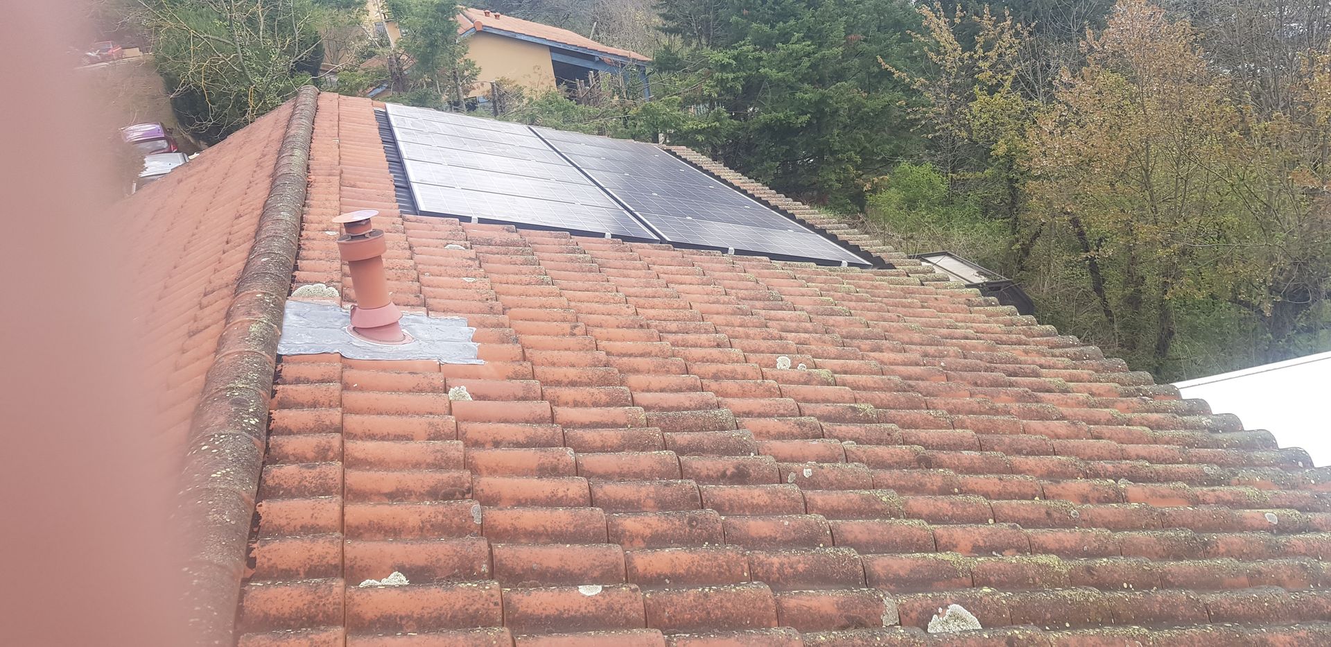 Toiture en tuiles de terre cuite avec panneaux solaires et cheminée.