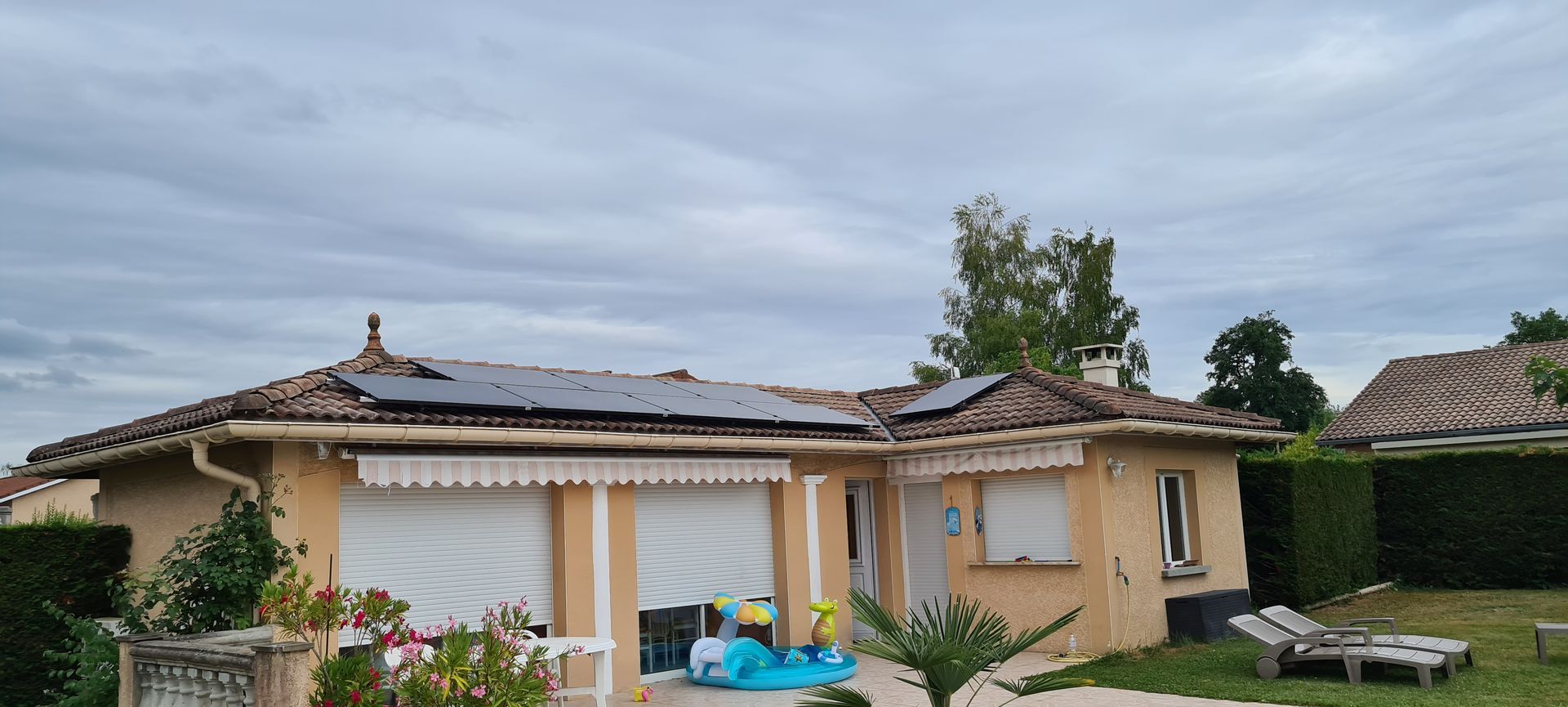 Maison avec panneaux solaires sur le toit et volets blancs ; ciel nuageux.
