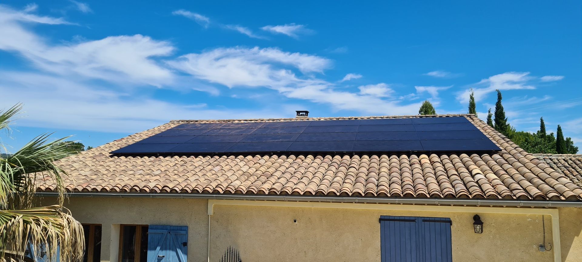 Panneaux solaires sur le toit en tuiles de terre cuite d'une maison claire, se détachant sur un ciel bleu.