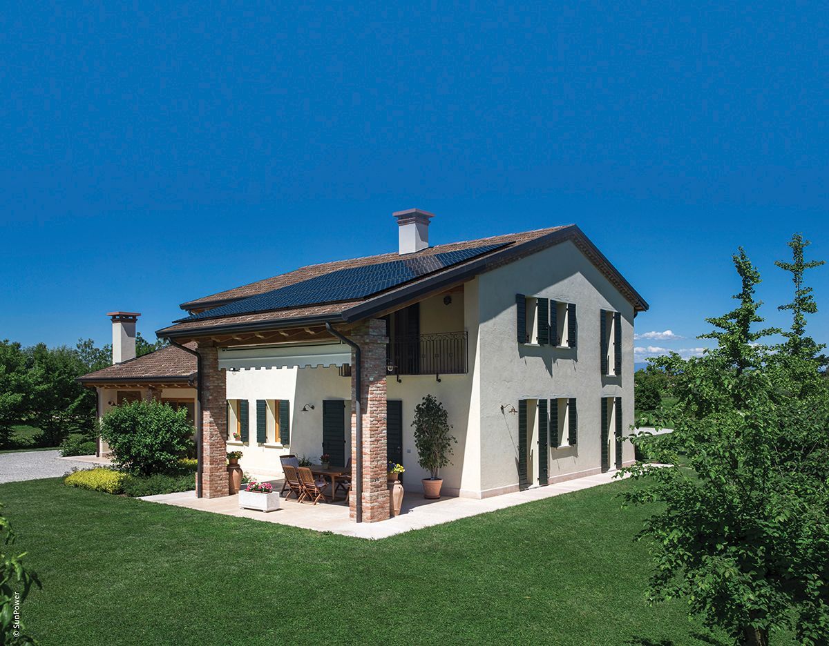 Maison à deux étages avec panneaux solaires sur le toit, pelouse verte, ciel bleu dégagé.