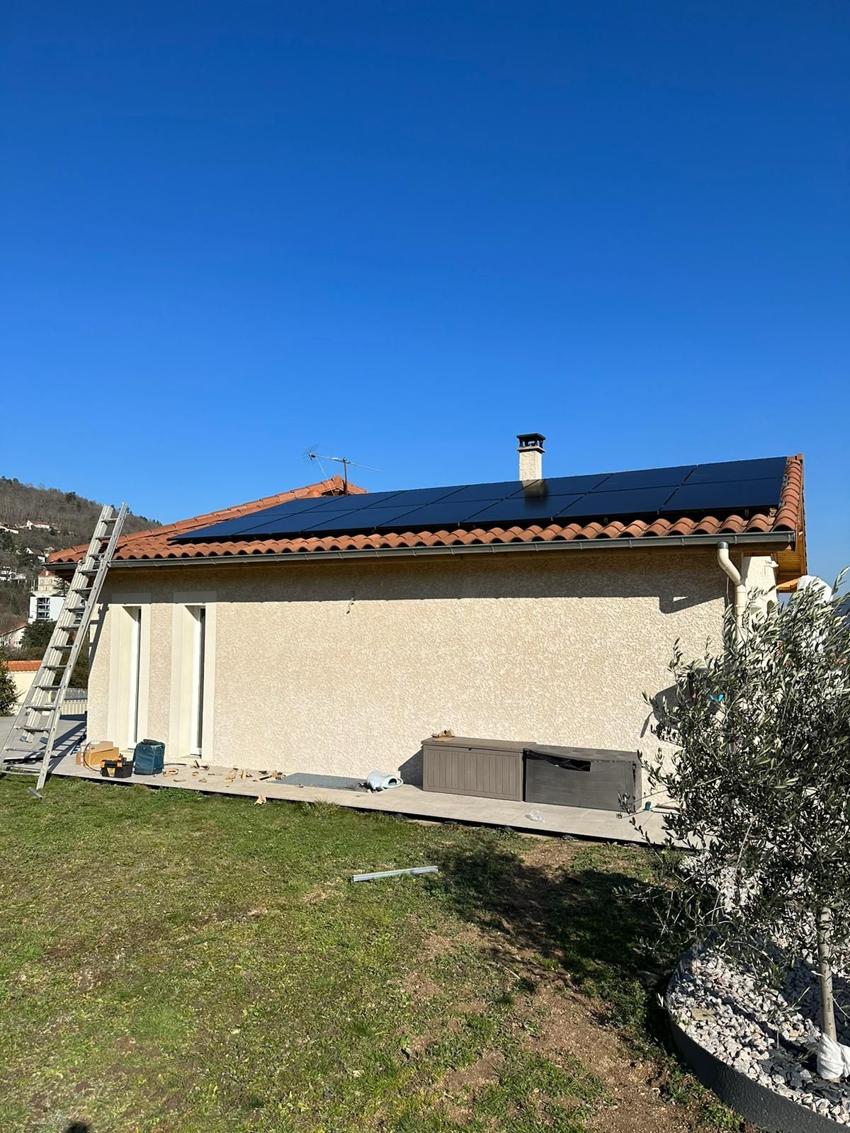 Maison avec panneaux solaires sur le toit, échelle appuyée contre celui-ci, par une journée ensoleillée.