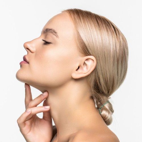 Mujer aplicándose crema hidratante en la cara, sonriendo sobre un fondo naranja.