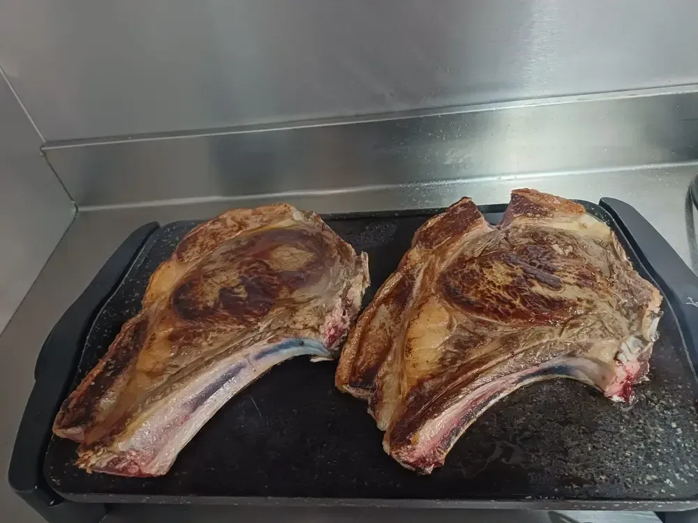 Dos filetes de costilla sellados en una parrilla negra, que muestran la corteza dorada y el hueso expuesto.