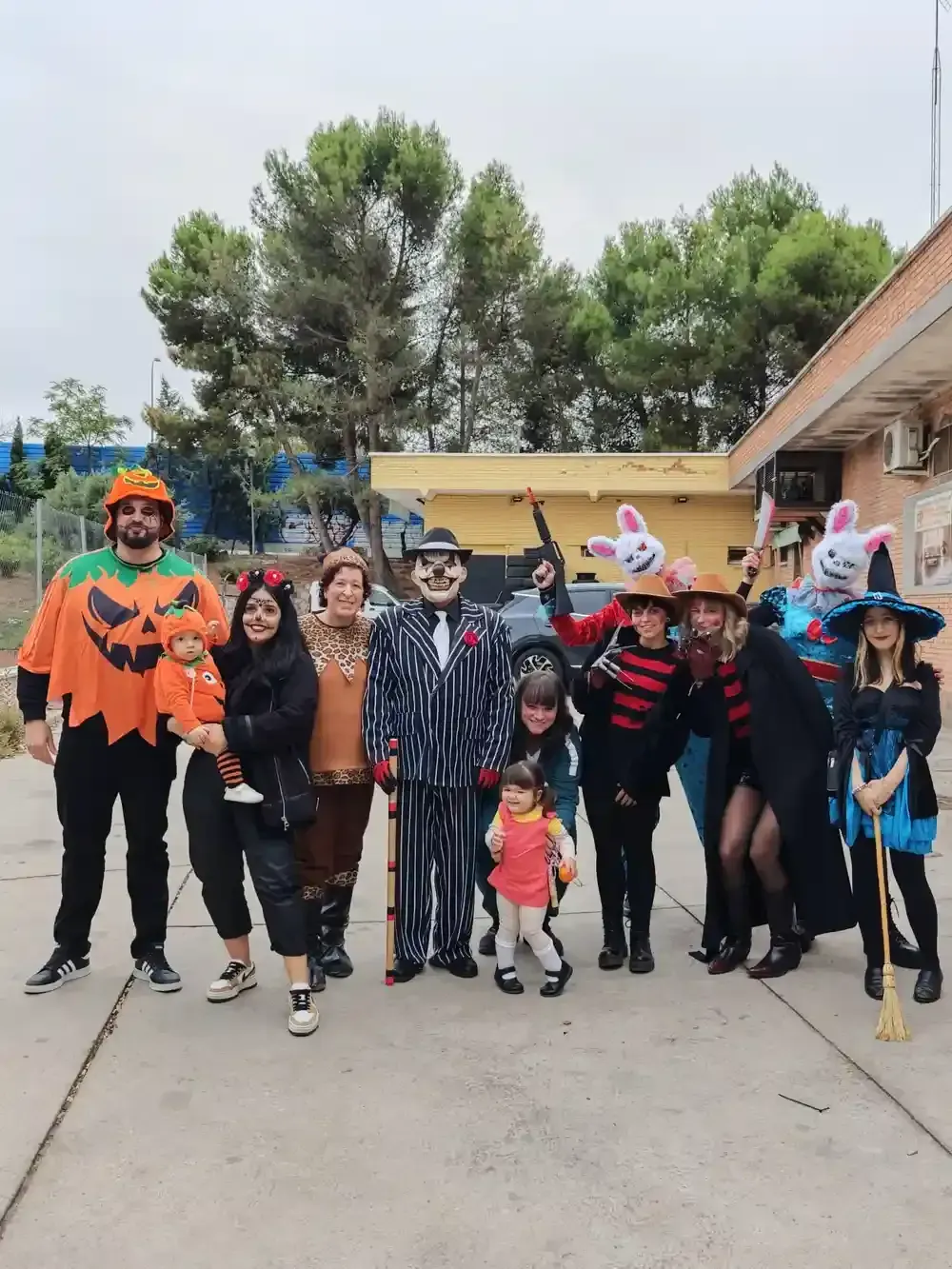 Grupo de personas disfrazadas de Halloween posando al aire libre; entre ellas una calabaza, una bruja y Freddy Krueger.