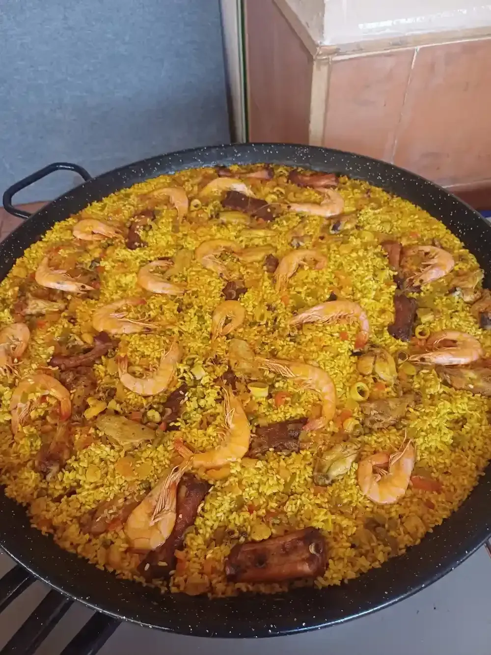 Paella en sartén grande negra. Arroz amarillo con camarones, carne y verduras.