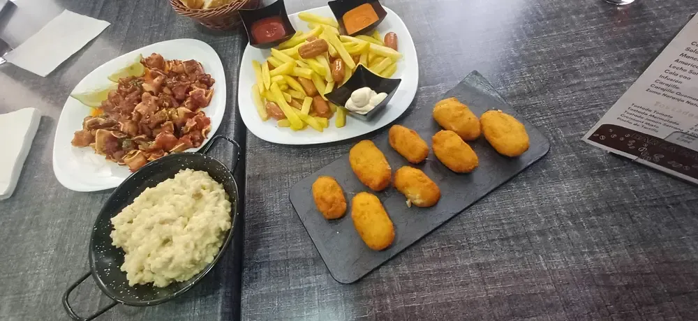 Una mesa con diversas tapas que incluyen croquetas, patatas fritas y otros platos.