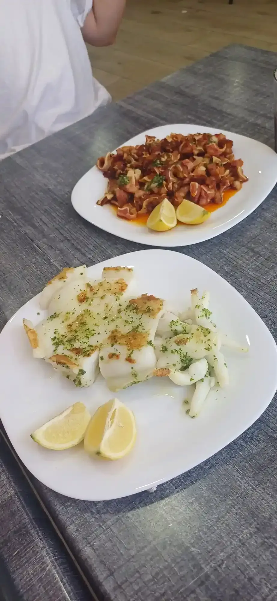Dos platos de comida sobre una mesa. Uno con carne cocida y limón, el otro con pescado a la plancha y limón.