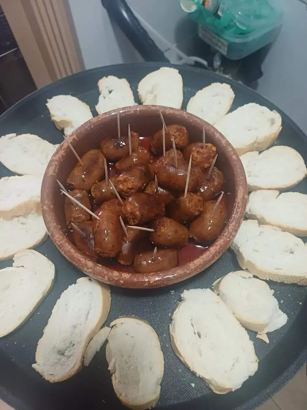 Un plato de tapas: pequeñas salchichas en un bol con palillos, rodeadas de rebanadas de pan tostado.