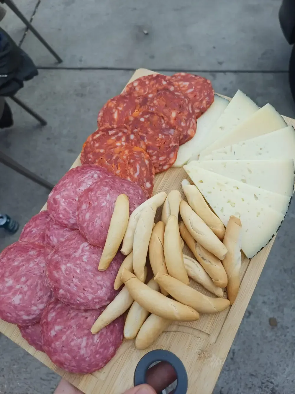 Tabla de embutidos: salami, chorizo, lonchas de queso y palitos de pan sobre madera.