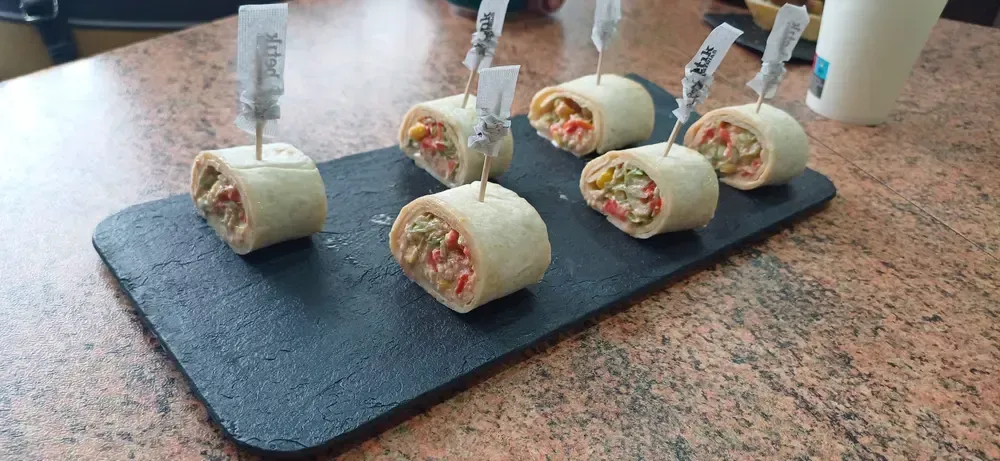 Wraps rellenos de ingredientes coloridos, ensartados y dispuestos sobre una pizarra negra.