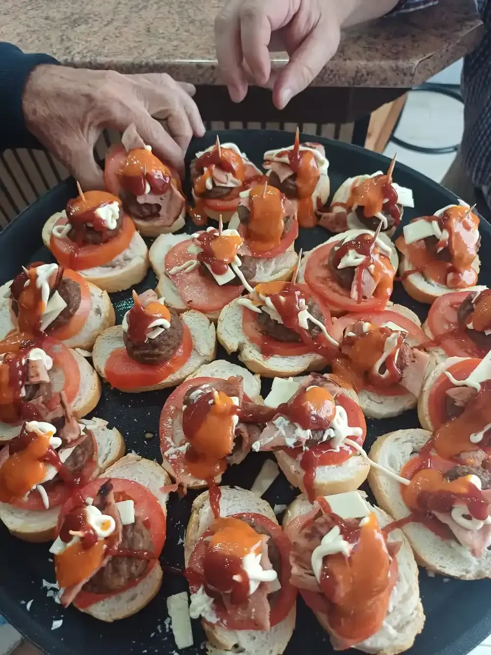 Bandeja de pequeños aperitivos: tomate, carne y salsa sobre pan, con las manos metidas dentro.