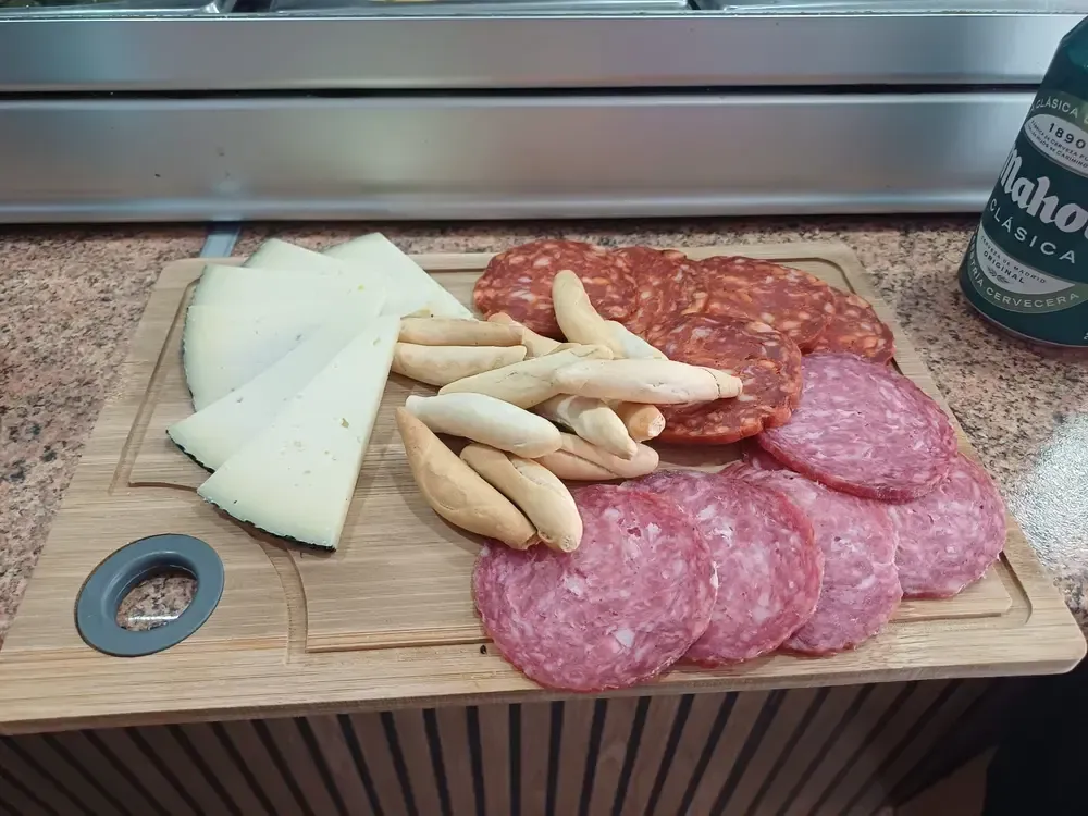 Tabla de embutidos: queso, palitos de pan, chorizo ​​y salami. Lata de cerveza al fondo.