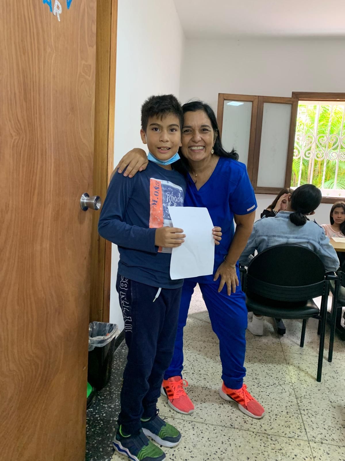 Un niño y una mujer sonríen, abrazados. Están dentro de casa, con un papel en la mano del niño.