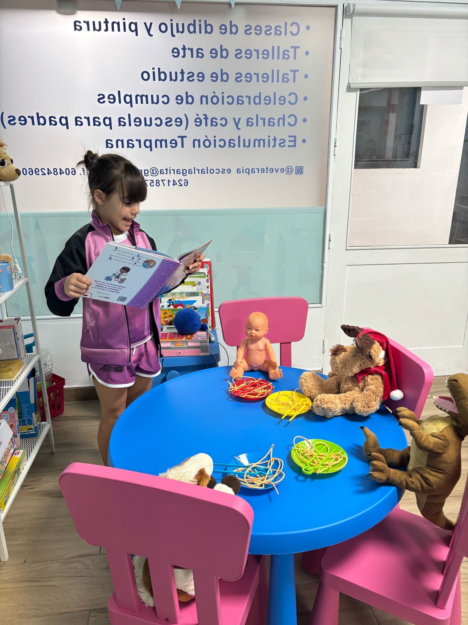 Una niña lee a los juguetes en una mesa azul en un salón de clases.