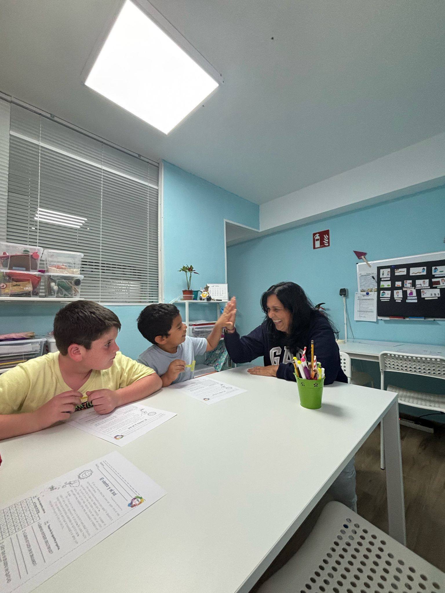 Dos niños y un profesor sentados en una mesa en un aula, chocando los cinco.