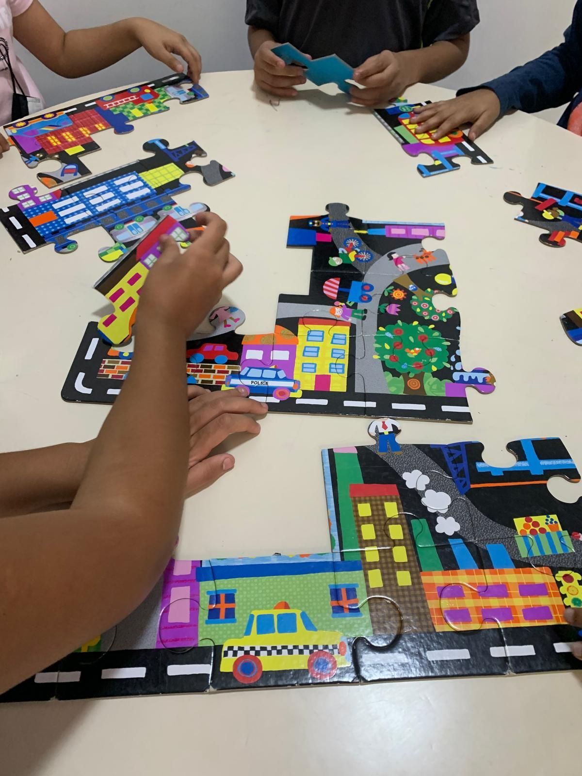 Niños armando un rompecabezas de ciudad colorido sobre una mesa blanca.