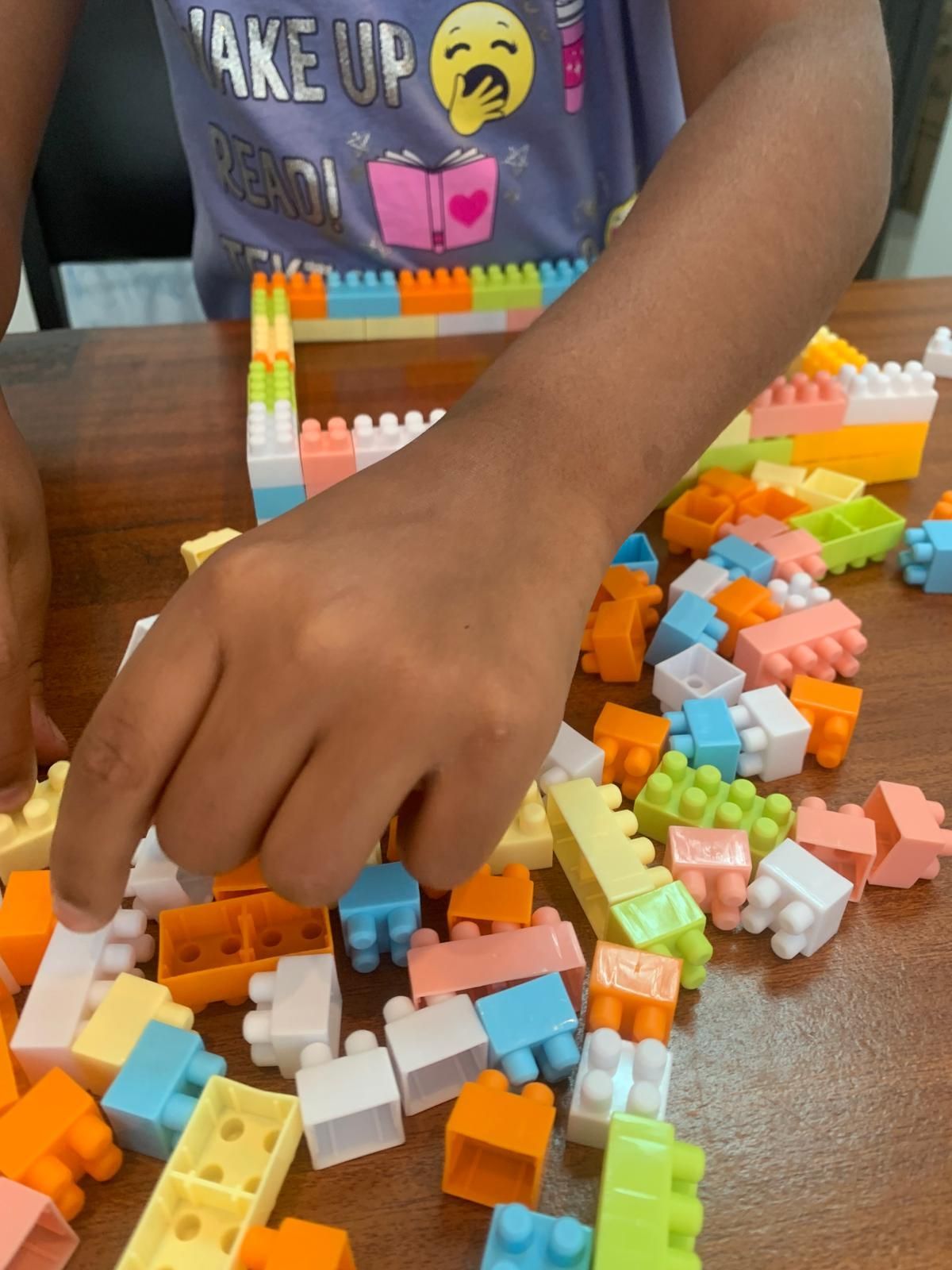 La mano de un niño alcanza bloques de construcción de colores sobre una mesa de madera. Una estructura está parcialmente construida.