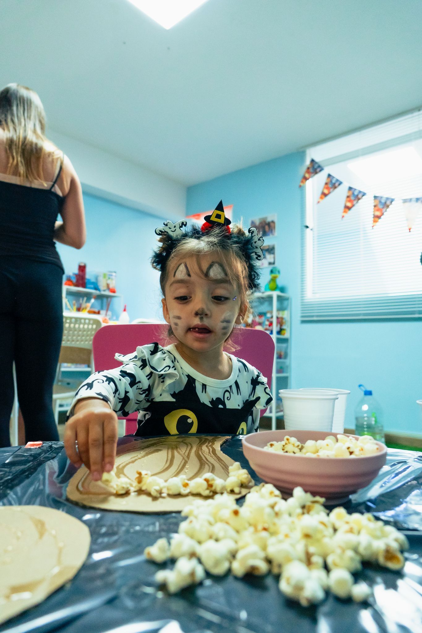 Una niña está sentada en una mesa con un tazón de palomitas de maíz.