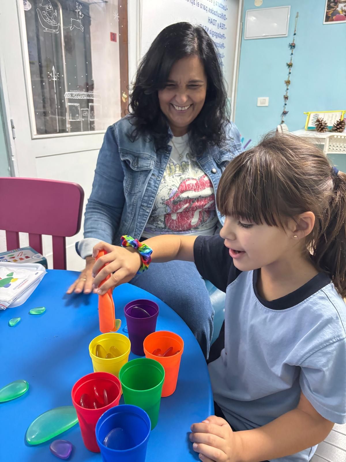 Una mujer y una niña están sentadas en una mesa jugando con tazas de colores.