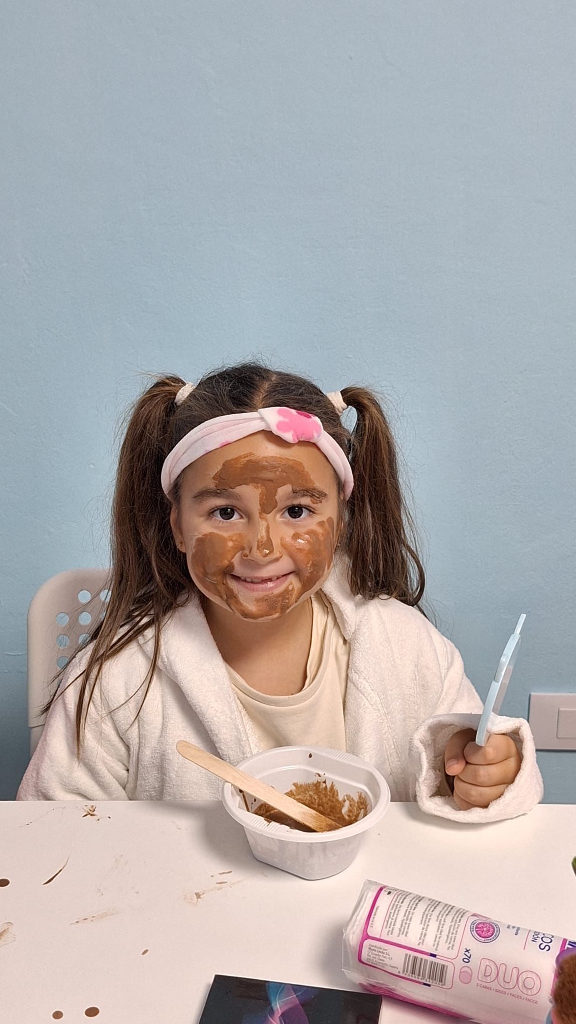 Una niña está sentada en una mesa con un plato de comida en su cara.