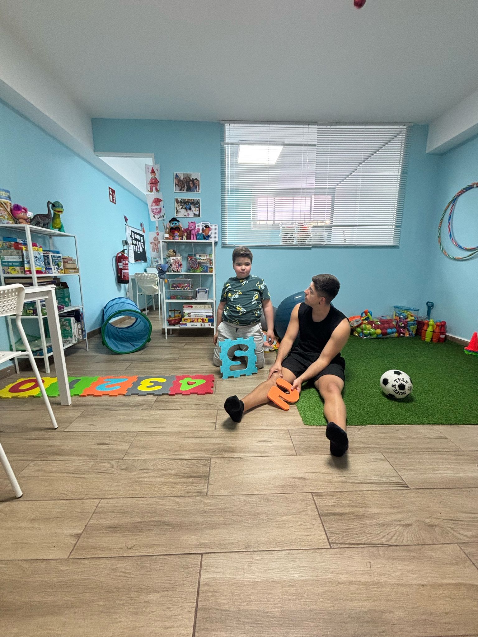 Hombre y niño jugando con letras y un balón de fútbol en una sala de juegos colorida.