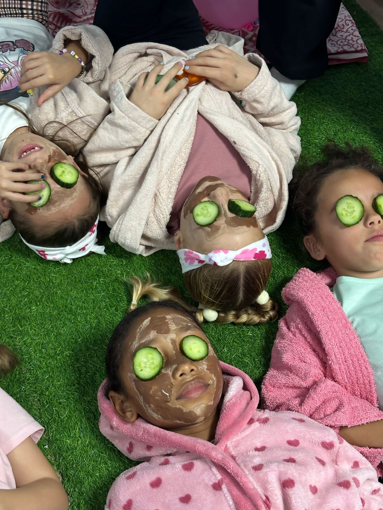Un grupo de niños están acostados en el suelo con rodajas de pepino en los ojos.