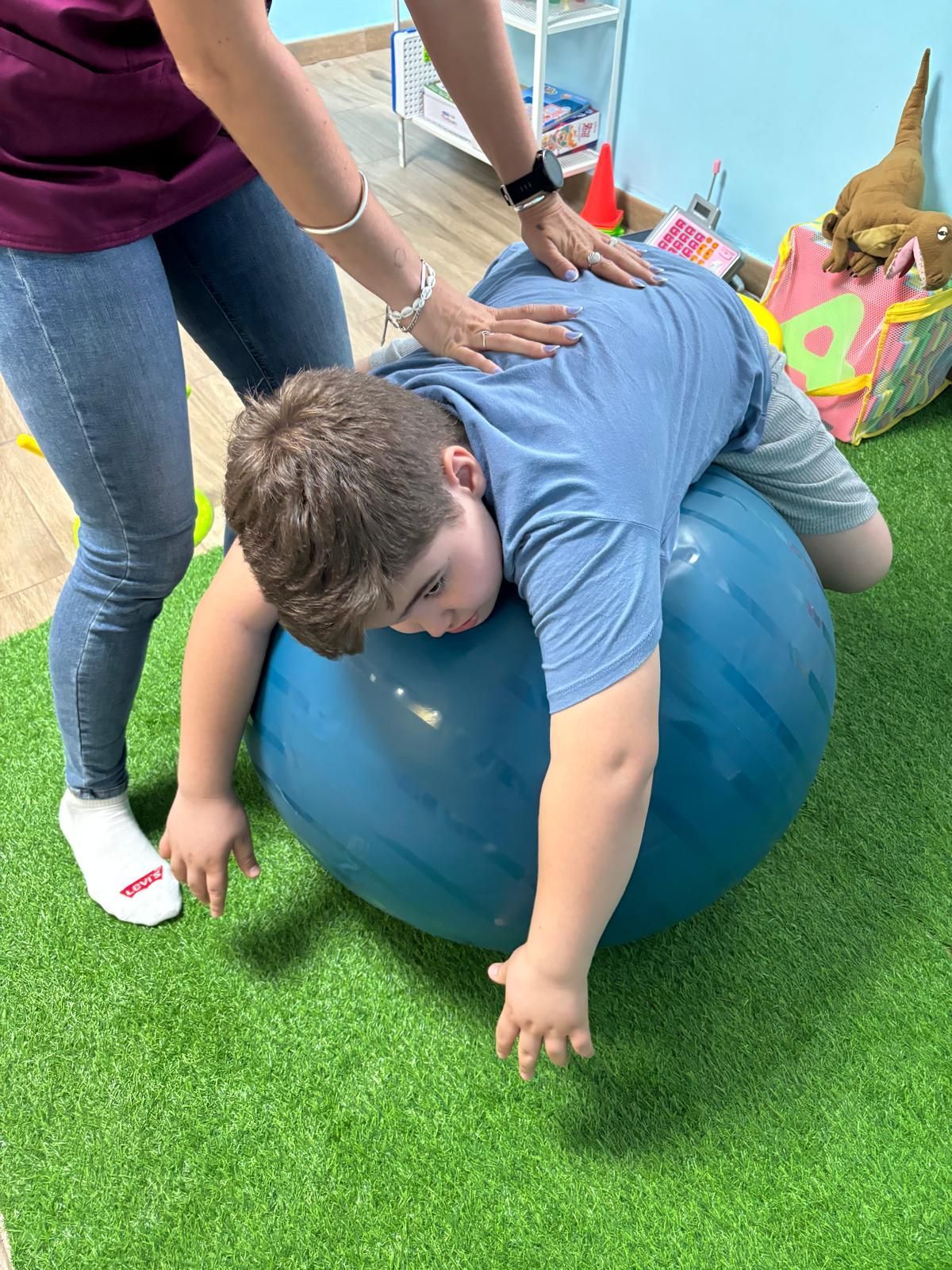 Un niño pequeño está acostado sobre una pelota de ejercicio azul.