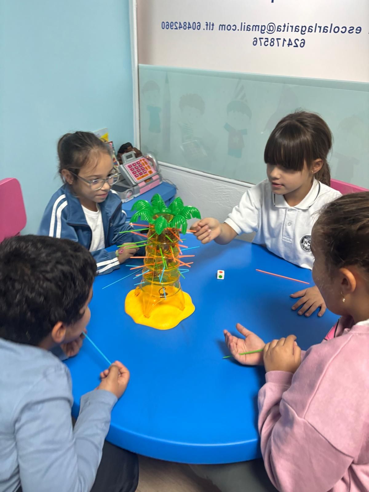 Niños jugando a un juego con temática de árboles en una mesa azul. Se muestran concentrados, con diversos tonos de piel y vestimenta.