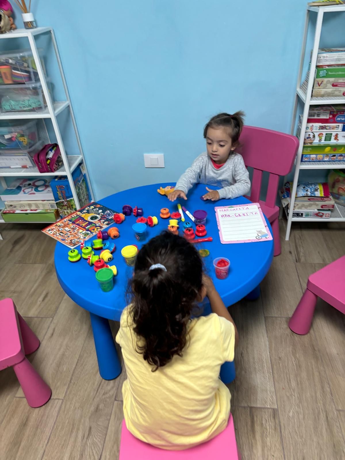 Dos niñas están sentadas en una mesa jugando con juguetes.