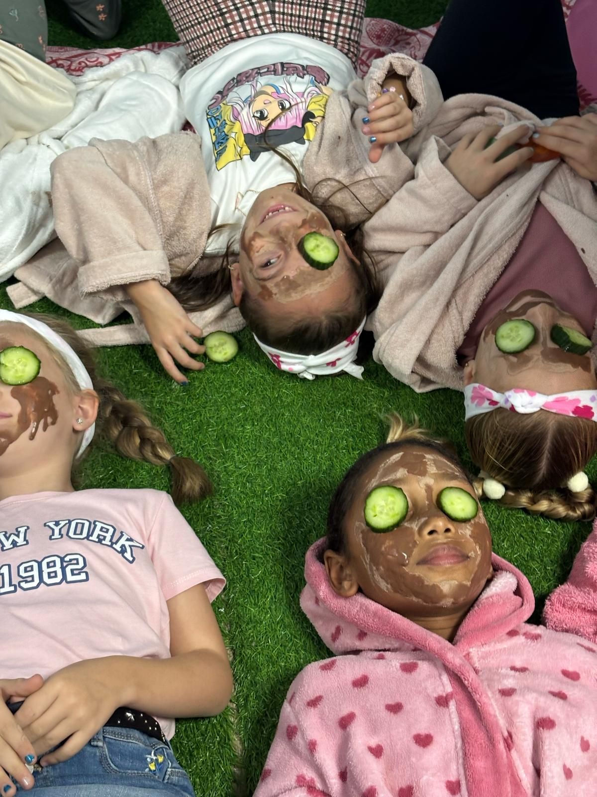 Un grupo de chicas jóvenes tumbadas en el césped con mascarillas y pepinos en los ojos.