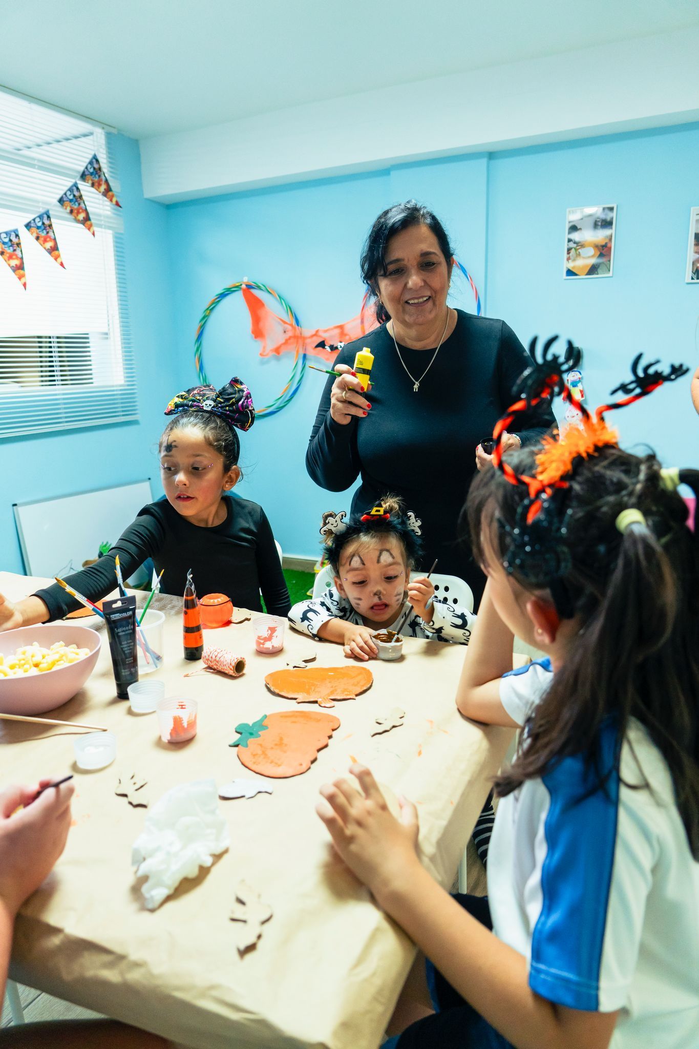 Un grupo de niños está sentado alrededor de una mesa con una mujer parada detrás de ellos.
