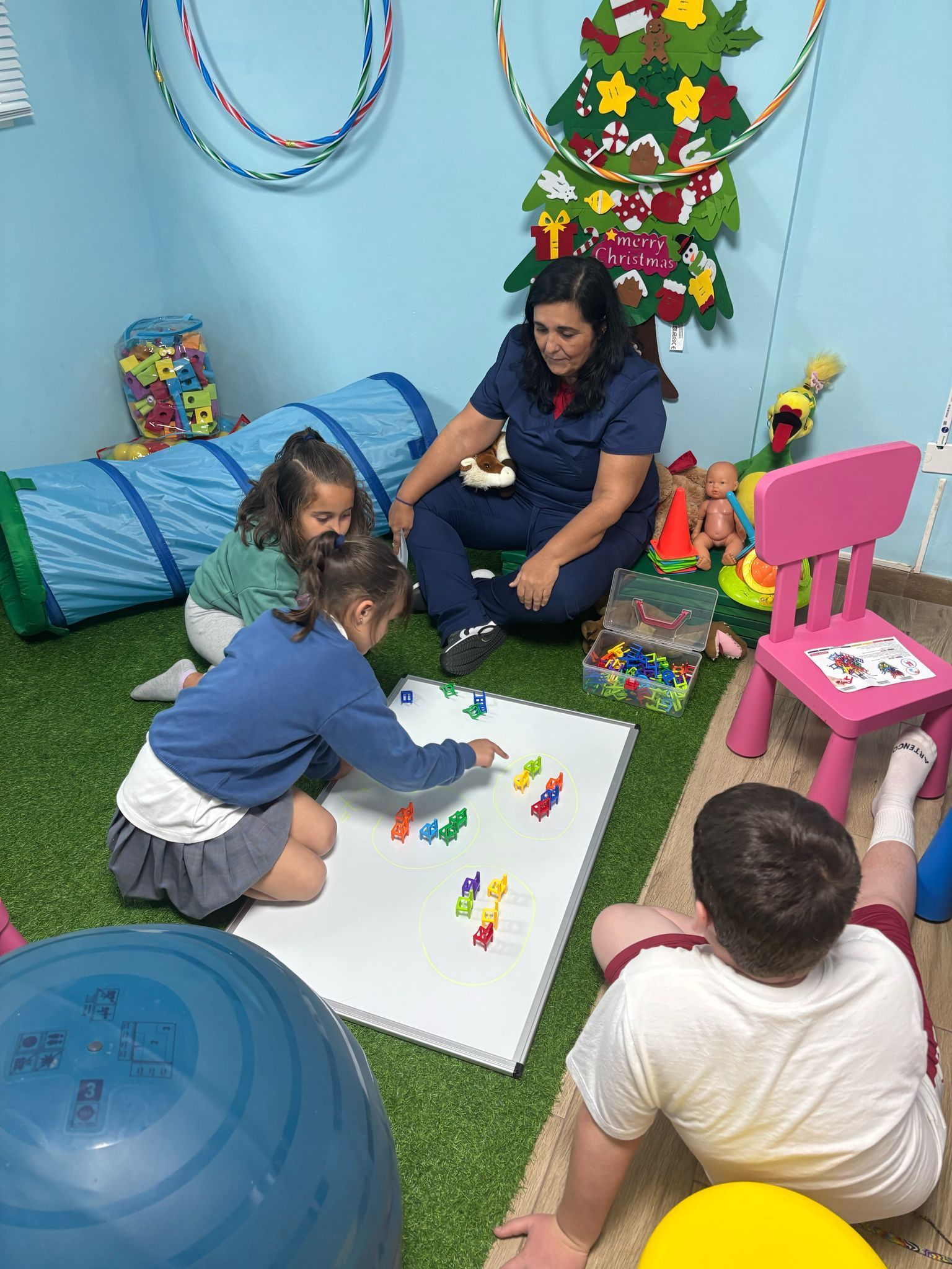 Niños y terapeuta en una sala de terapia con un árbol de Navidad. Juegan con objetos de colores.