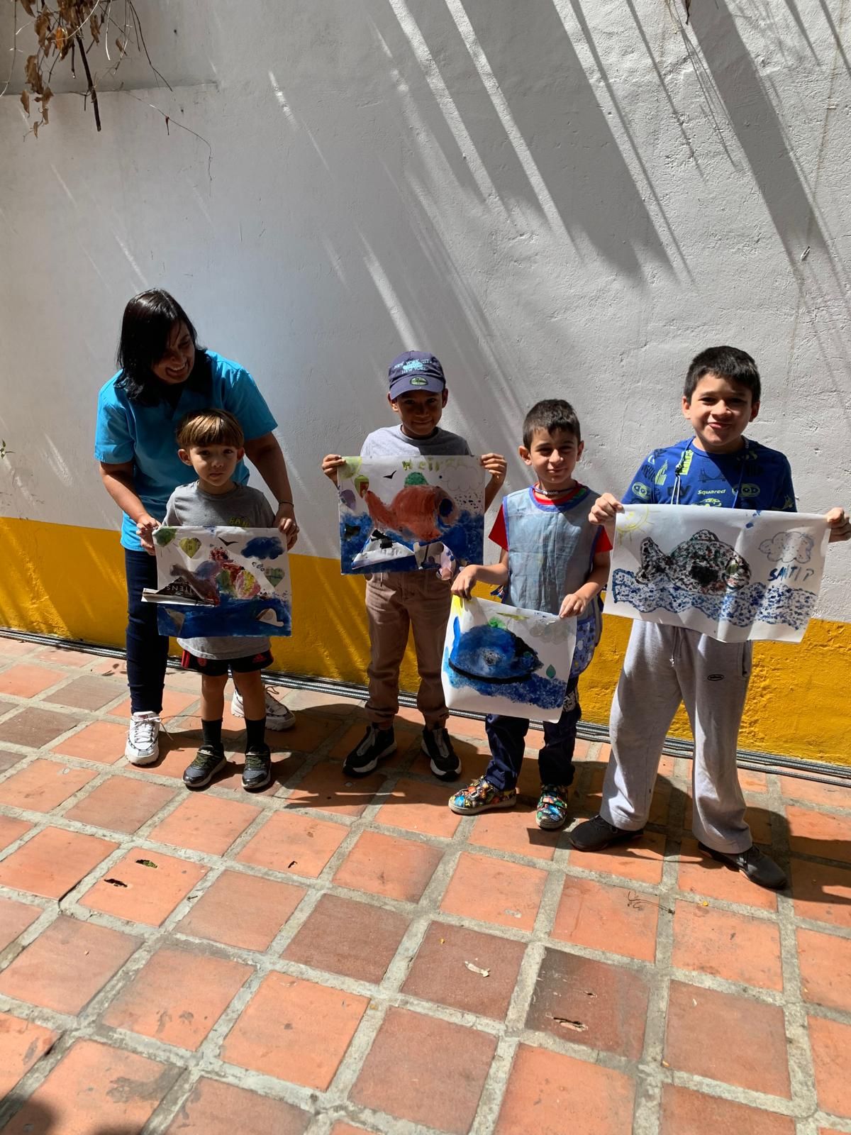 Grupo de niños y una mujer exhibiendo sus obras de arte al aire libre.