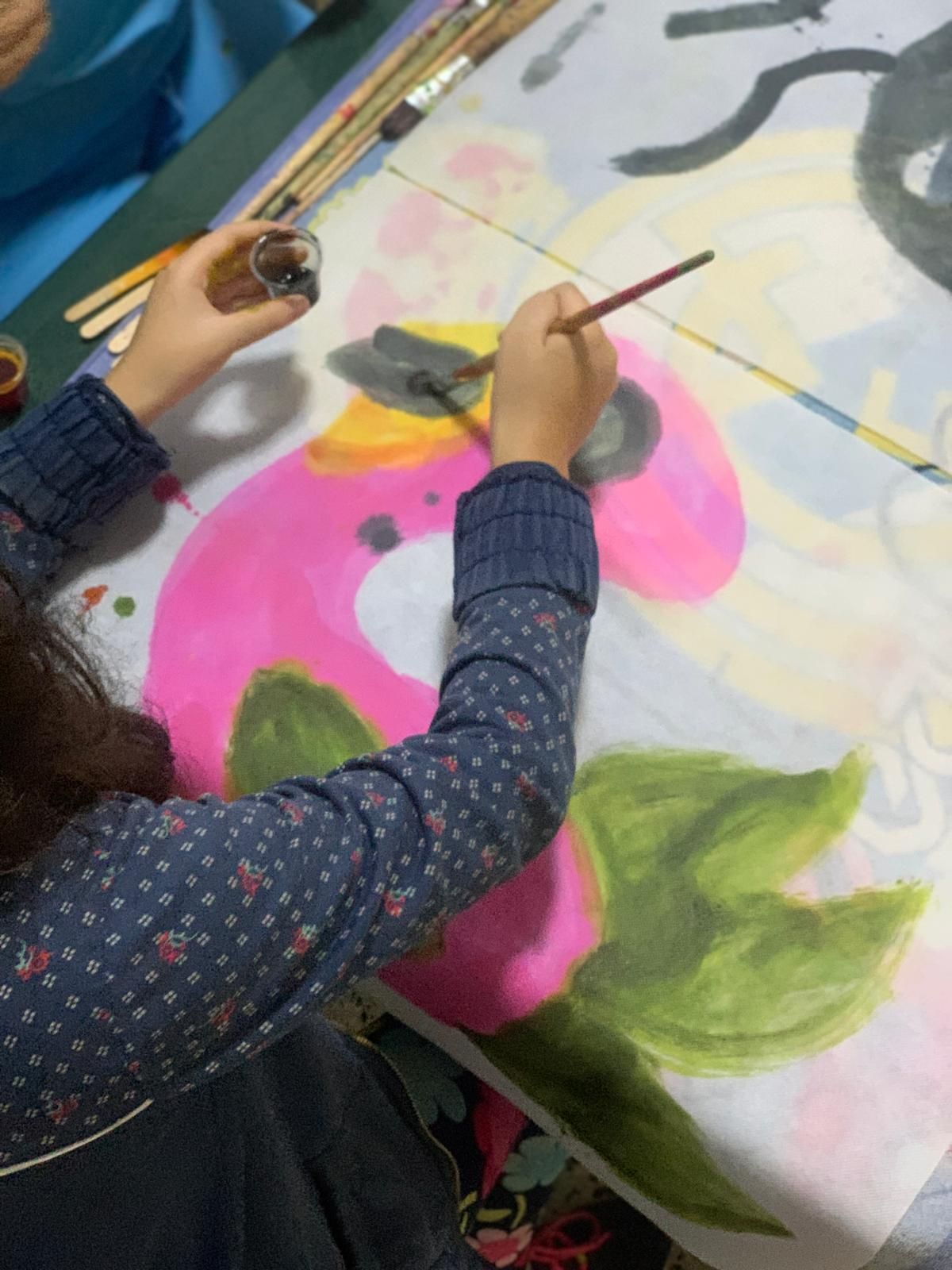 Niño pintando una gran flor rosa con hojas verdes, usando pintura negra en los pétalos.