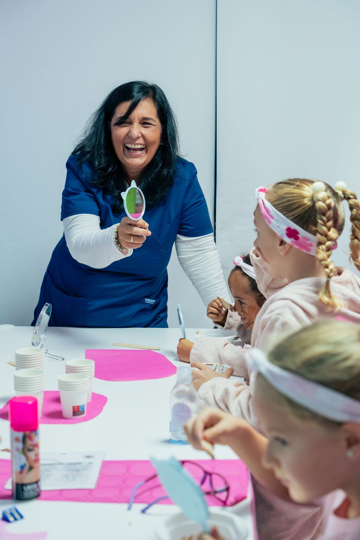 Una mujer está de pie junto a un grupo de chicas jóvenes sentadas en una mesa.