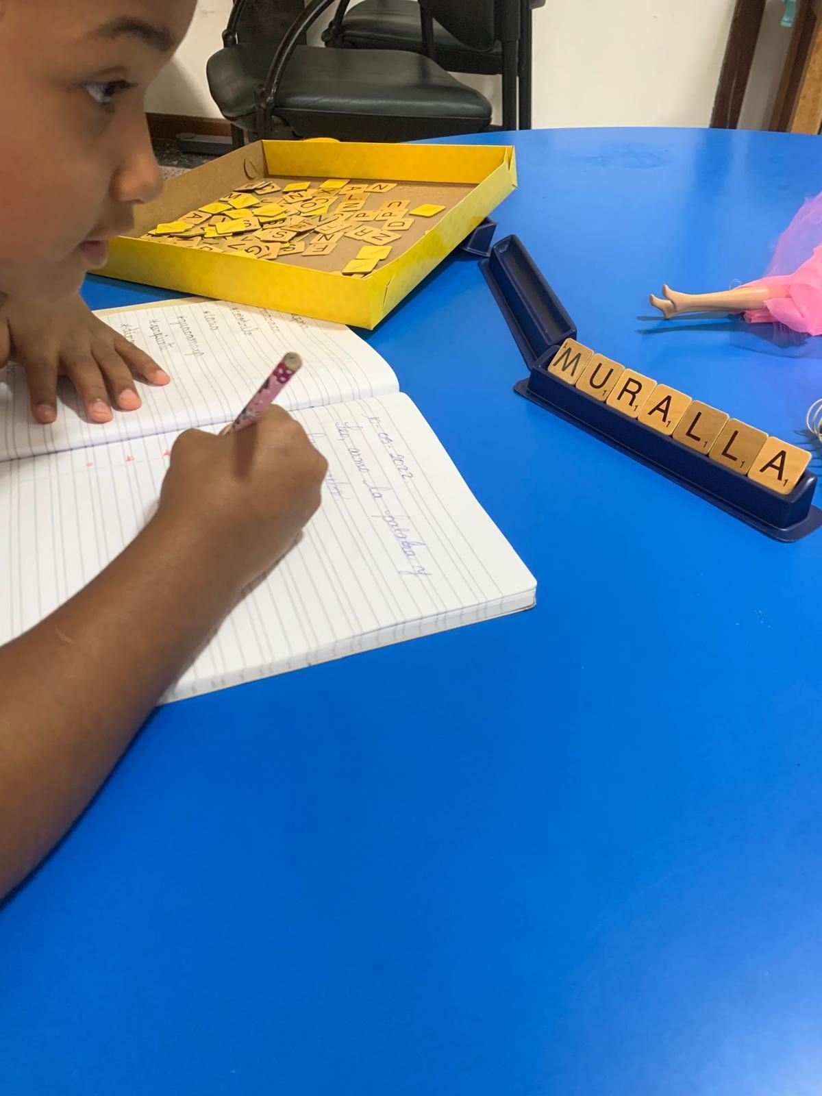 Niña escribiendo en un cuaderno, con fichas de letras que forman la palabra
